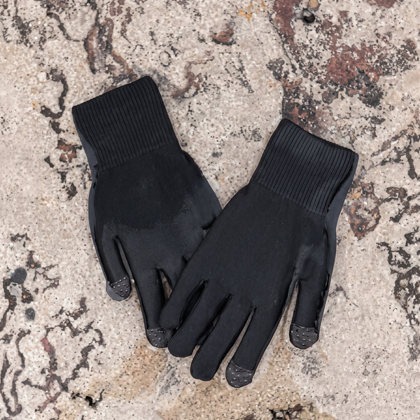 Black HEMY waterproof gloves lying on a rocky shore